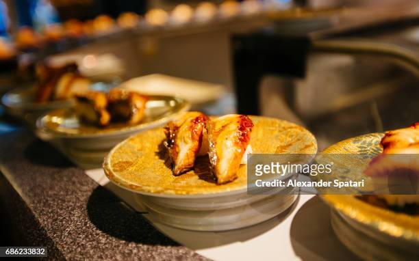 plate with unagi (eel) nigiri at the conveyor belt in a sushi bar, tokyo, japan - sushi train stock pictures, royalty-free photos & images