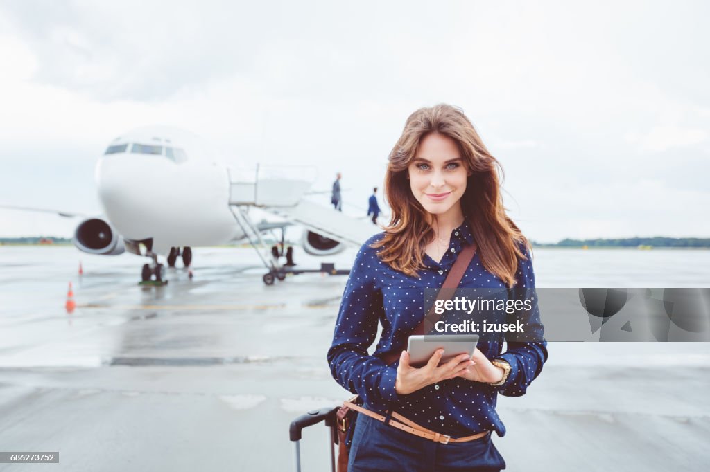 Beautiful business woman with digital tablet in front of airplane