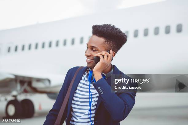 jonge afrikaanse zakenman met behulp van mobiele telefoon op luchthaven - airport hipster travel stockfoto's en -beelden