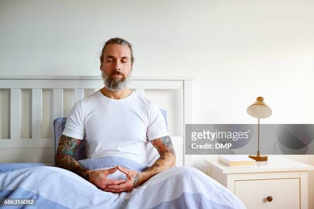 mature man sitting peacefully on bed - man meditating stock pictures, royalty-free photos & images
