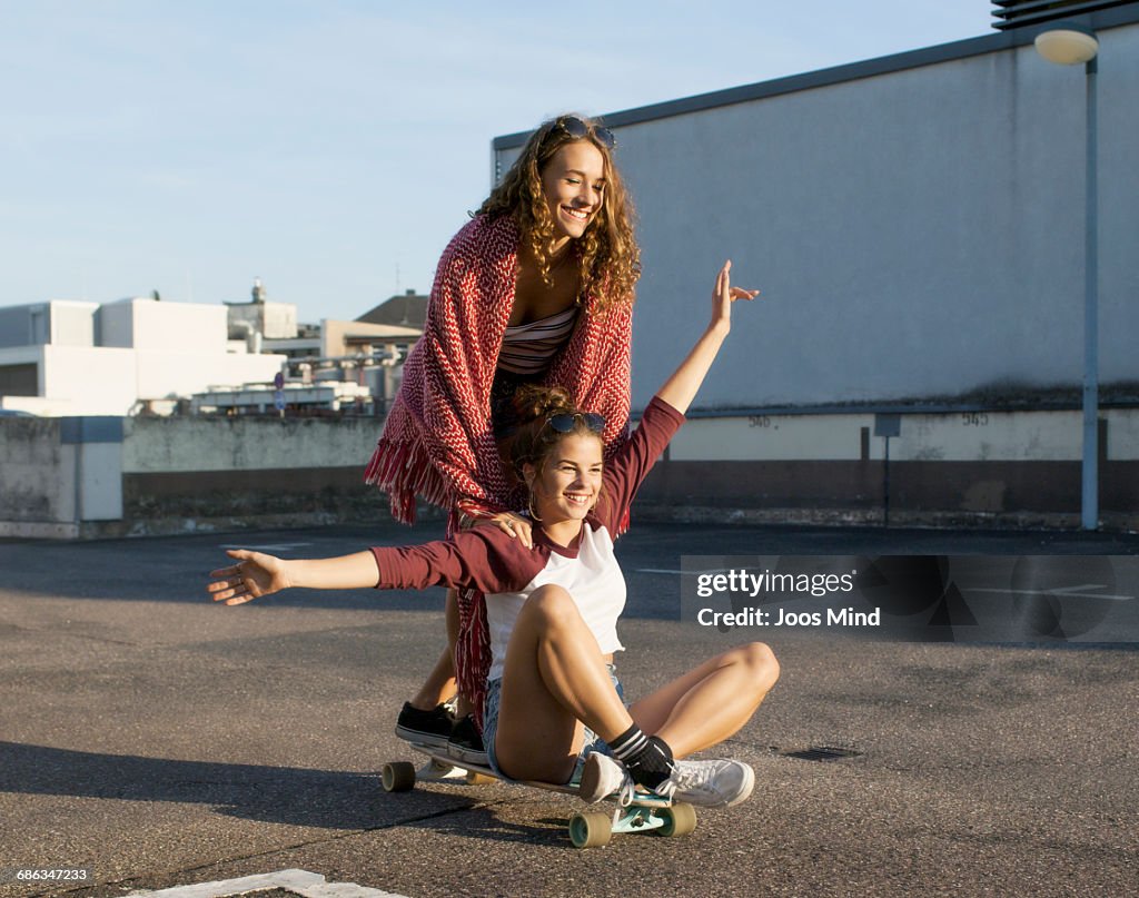Teenage girls using skateboard on rooftop car park