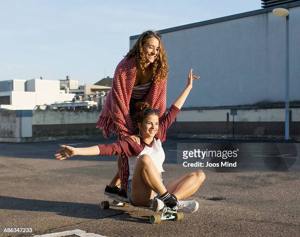 teenage girls using skateboard on rooftop car park - fun stock-fotos und bilder