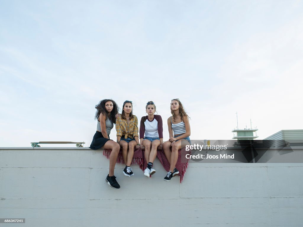 Teenage girls sitting on rooftop wall