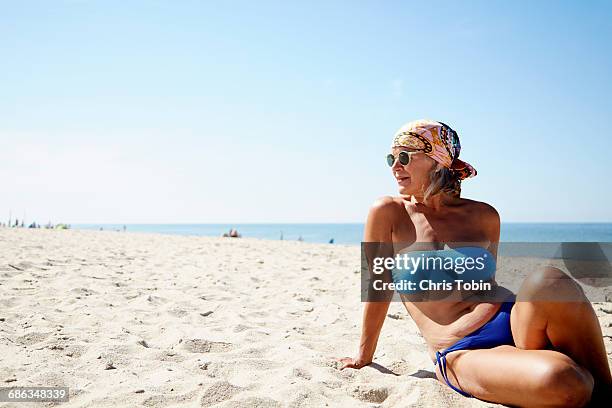 older woman lounging on the beach - old woman in swimsuit stock-fotos und bilder