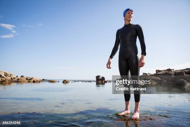 mid adult woman standing in her swimming wetsuit - wetsuit stock pictures, royalty-free photos & images