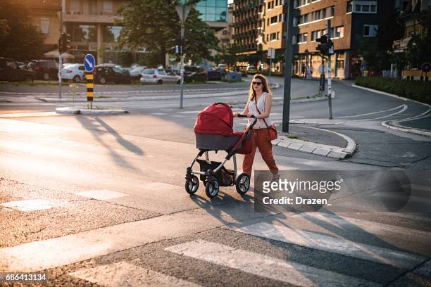 young mother walking across the pedestrian crosswalk - stroller stock pictures, royalty-free photos & images