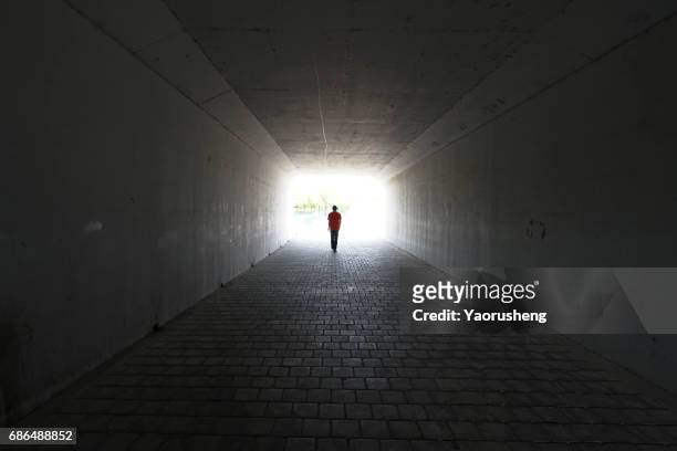 silhouette of person walking out of  a tunnel. light at end of tunnel - tod stock-fotos und bilder