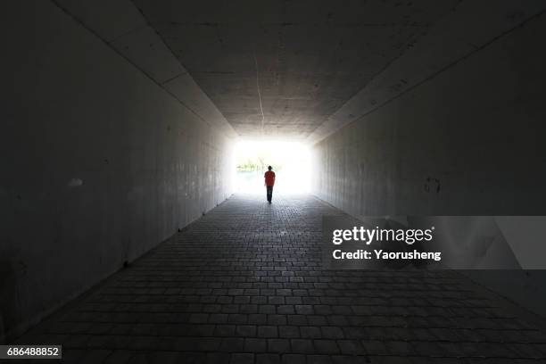 silhouette of person walking out of a tunnel. light at end of tunnel - tunnel stock-fotos und bilder