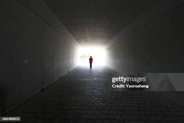 silhouette of person walking out of  a tunnel. light at end of tunnel - doden stockfoto's en -beelden