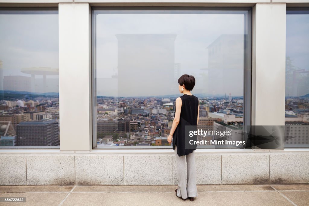 A woman standing looking over a city from a high viewing point.