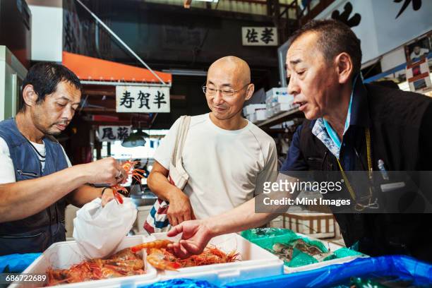 A traditional fresh fish market in Tokyo. Two people selecting shellfish for a customer to buy, filling a bag from boxes of prawns.