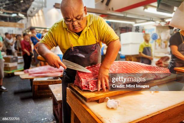 a traditional fresh fish market in tokyo. a fishmonger working filleting a large fish on a slab. people in the background. - fish market stock pictures, royalty-free photos & images