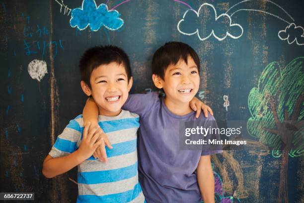 children in school. two boys standing with their arms around each others shoulders by a chalkboard. - blackboard visual aid 個照片及圖片檔