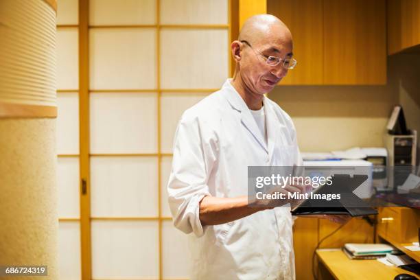 a chef in a small commercial kitchen, an itamae or master chef using a digital tablet. - 郷土料理　日本 ストックフォトと画像