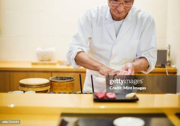 a chef working in a small commercial kitchen, an itamae or master chef presenting a fresh plate of sushi. - sushi chef stock pictures, royalty-free photos & images