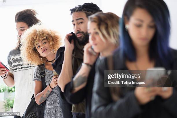 young people standing in line using smartphones - waiting in line stock-fotos und bilder