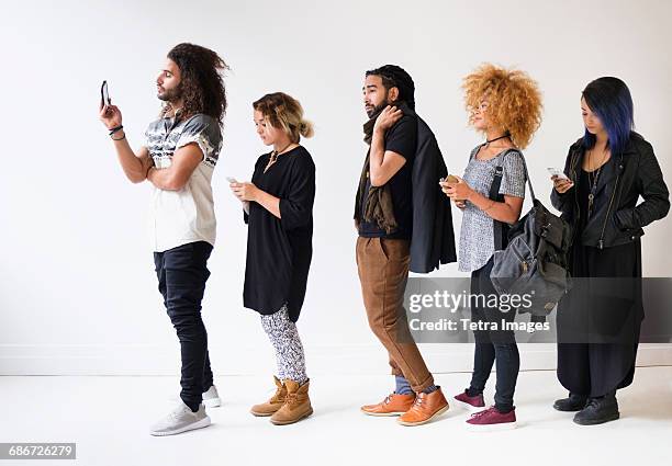 young people standing in line using smartphones - waiting in line stock-fotos und bilder