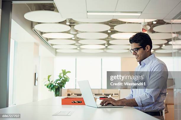 businessman working at high desk using laptop - indian ethnicity fotografías e imágenes de stock