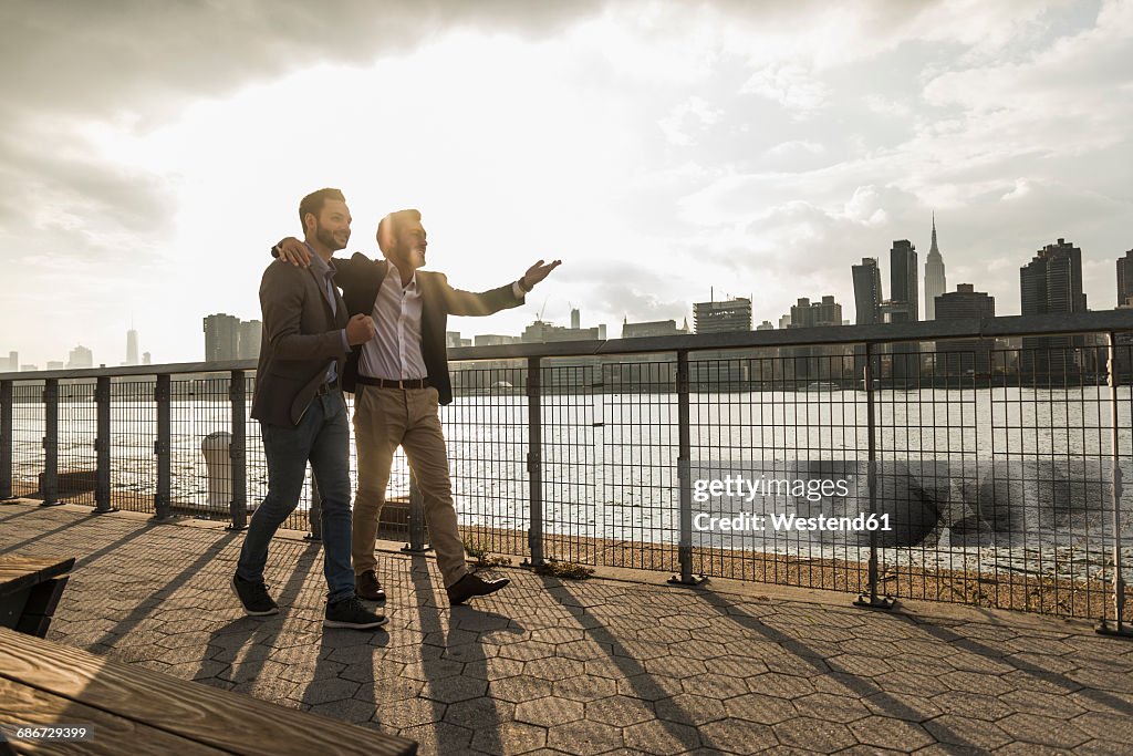 USA, New York City, two businessmen walking together along East River