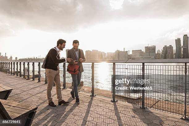usa, new york city, two young men walking along east river looking at cell phone - panorama nyc day 2 foto e immagini stock