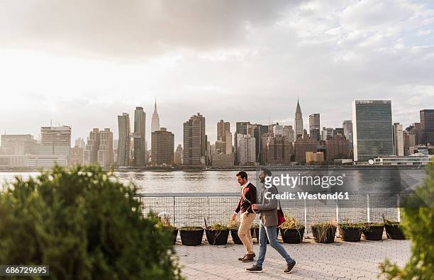 usa, new york city, two young men walking along east river - walking side view stock-fotos und bilder
