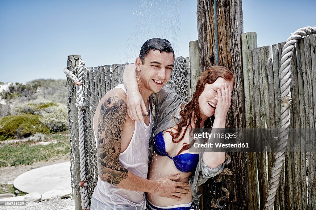 Young couple taking shower on the beach with clothes