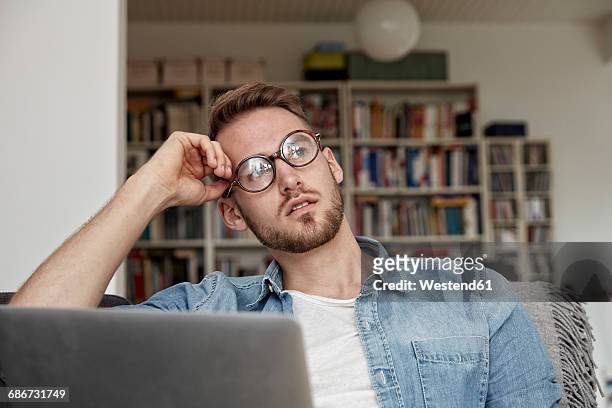 portrait of pensive man with laptop in the living room - beschaulichkeit stock-fotos und bilder