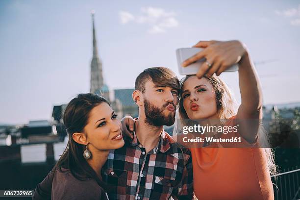 austria, vienna, three friends taking selfie on rooftop terrace with stephansdom in the background - stephansplatz stock pictures, royalty-free photos & images