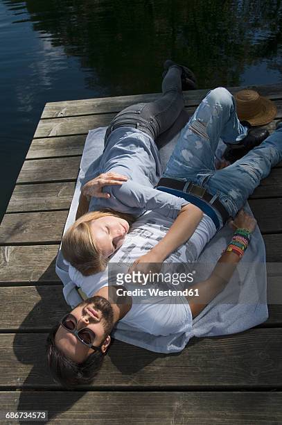 relaxed young couple lying on jetty at a lake - couple jetty stock pictures, royalty-free photos & images