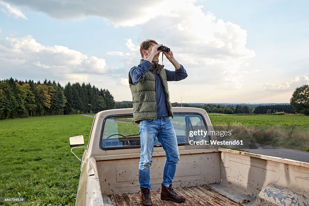Man standing on pick up truck looking through binoculars
