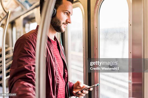 young man in subway wearing headphones - subway stock-fotos und bilder