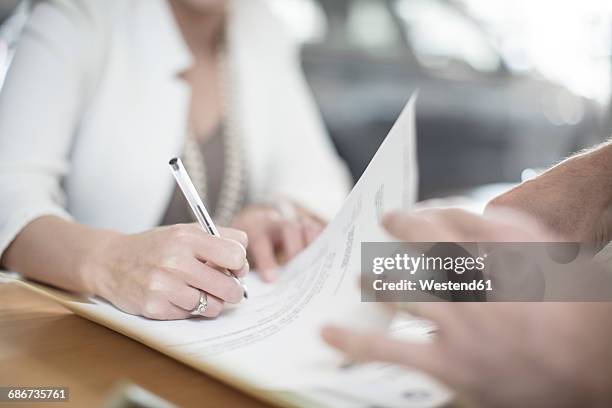 woman signing contract at desk at car dealership - firma foto e immagini stock