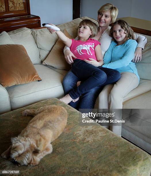 "mother and daughters sitting on sofa, watching tv together" - family tv pet stock pictures, royalty-free photos & images