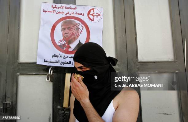 Palestinian demonstrator holds an onion used against tear gas in front of a placard bearing a picture of US President Donald Trump, denouncing his...