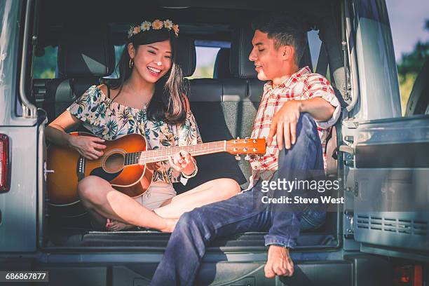 couple sitting in back of car playing guitar - west asia stock-fotos und bilder