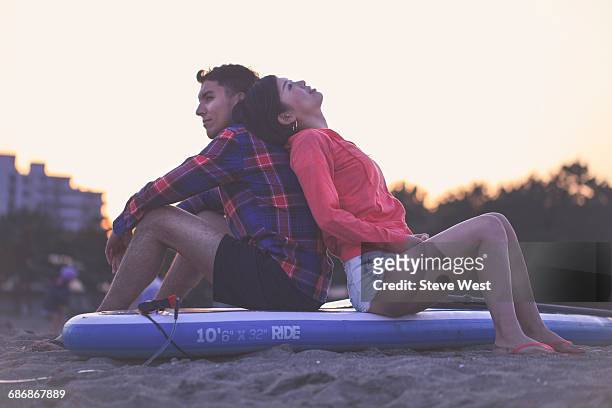 young couple relaxing on paddleboard at sunset - west asia stock-fotos und bilder
