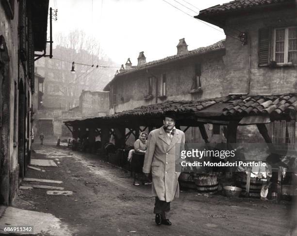 Belgian writer Georges Simenon, smoking a pipe, walking in the dirt road of Vicolo Lavandai. Milan, 1957