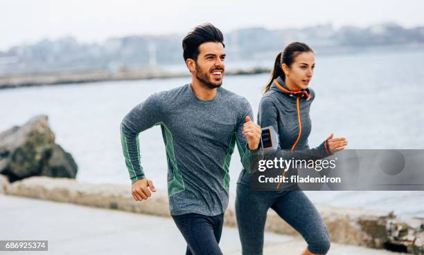 amici che fanno jogging in mare - couple running on beach foto e immagini stock