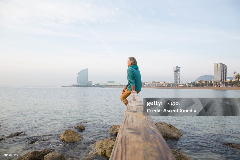 Man relaxes on waterfront rail, looks to sea