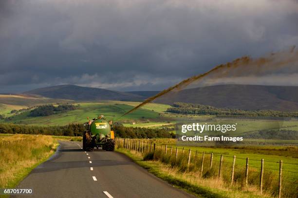 Farmer on road shooting slurry from spreader over fence into field to avoid damage to wet land. Trough of Bowland - Lancashire.