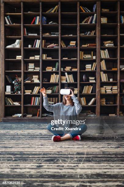 glückliche frau mit vr-brille vor bücherregalen - jugendkultur sitzen konsole stock-fotos und bilder