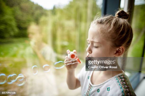 girl blowing soap bubbles at the window - people inside bubbles stock-fotos und bilder