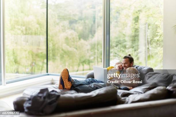 happy father with two children looking at laptop on the couch - wireless technology family stock pictures, royalty-free photos & images