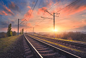 Railroad and beautiful sky at sunset. Industrial landscape with railway station, colorful blue sky with red clouds, trees and green grass, yellow sunlight in summer. Railway junction. Heavy industry
