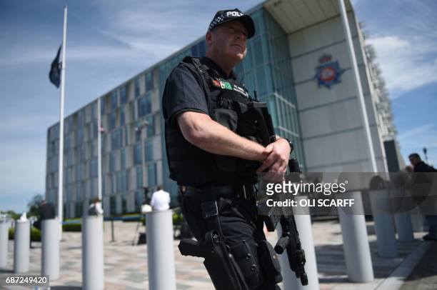 Flags fly at half-mast as an armed British Police officers walks on patrol with his weapon outside of Greater Manchester Police force's headquarters...