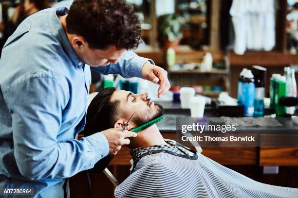 barber trimming up clients beard after shave in barber shop - barbier stockfoto's en -beelden