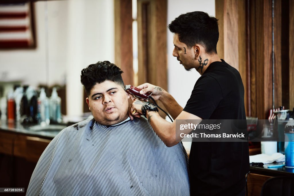 Barber cutting clients sideburns with trimmer in barber shop