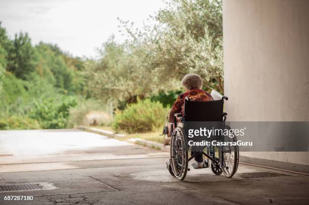 achteraanzicht van senior vrouw op de rolstoel in de garage-corridor - residential care stockfoto's en -beelden