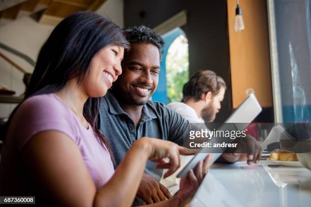 multi-ethnic couple at a cafe using a tablet computer - man atm smile stock pictures, royalty-free photos & images