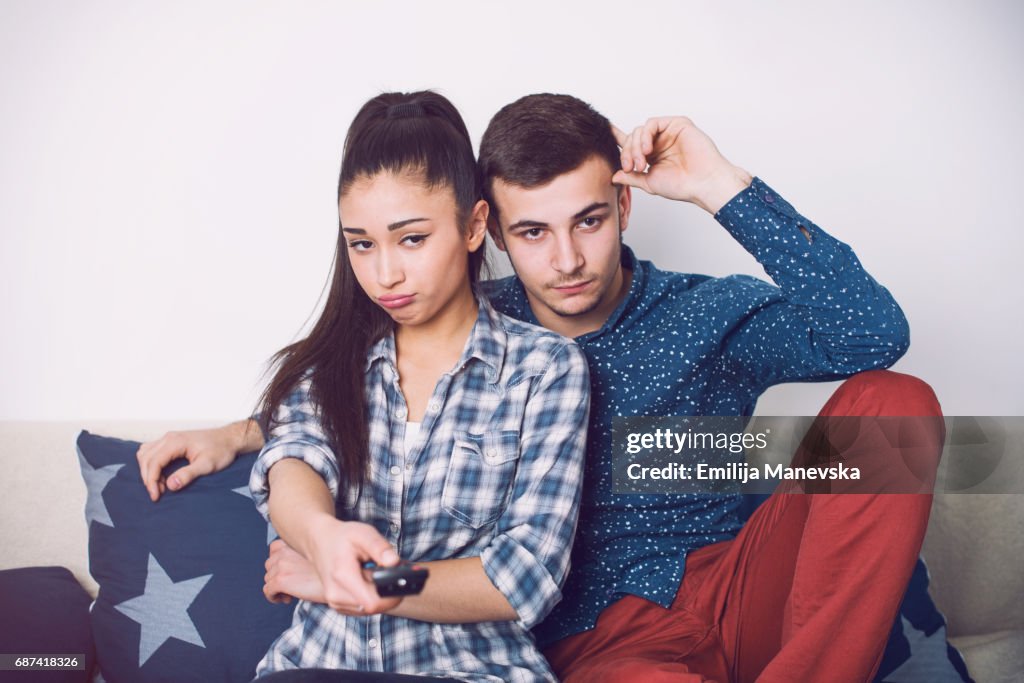 Young couple watching boring television program